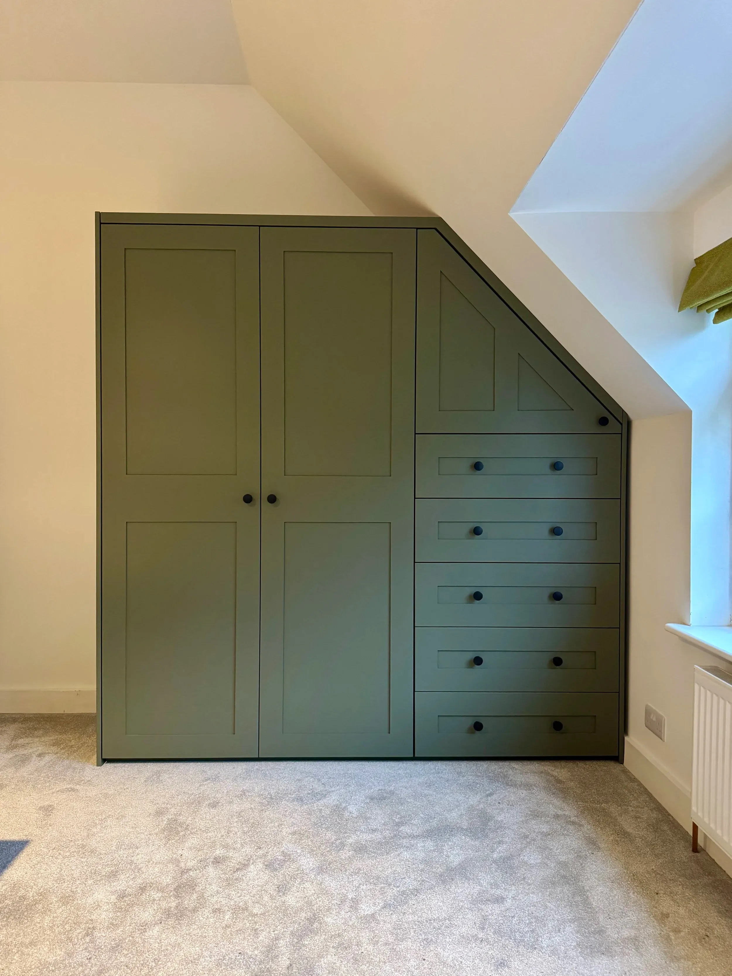 Green fitted wardrobe shaped to the eaves